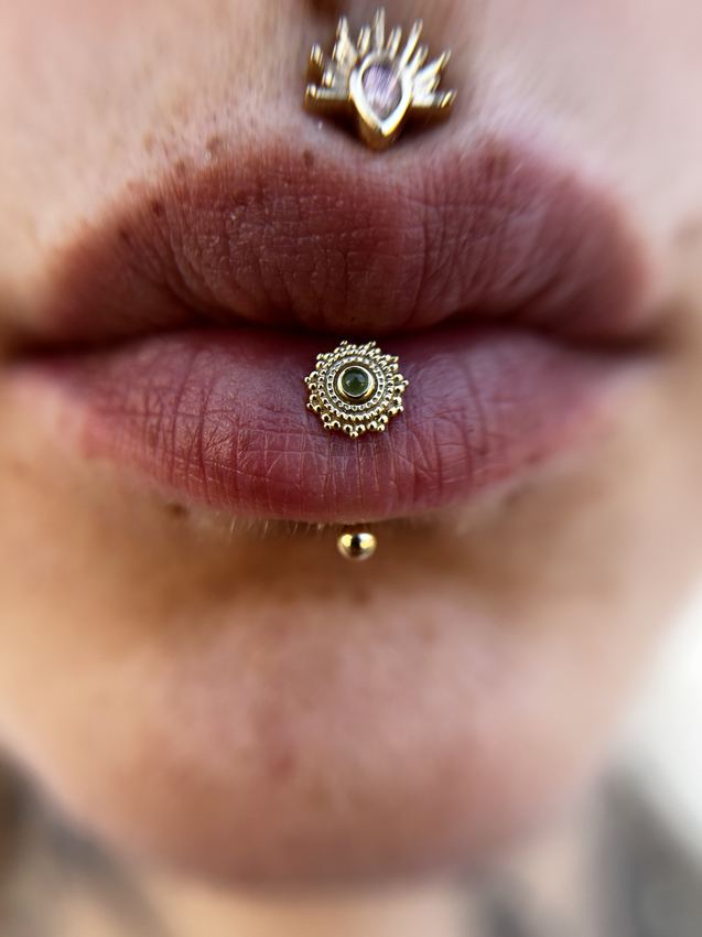 Piercing philtrum con gema y labret vertical en el labio inferior, con joyería de oro