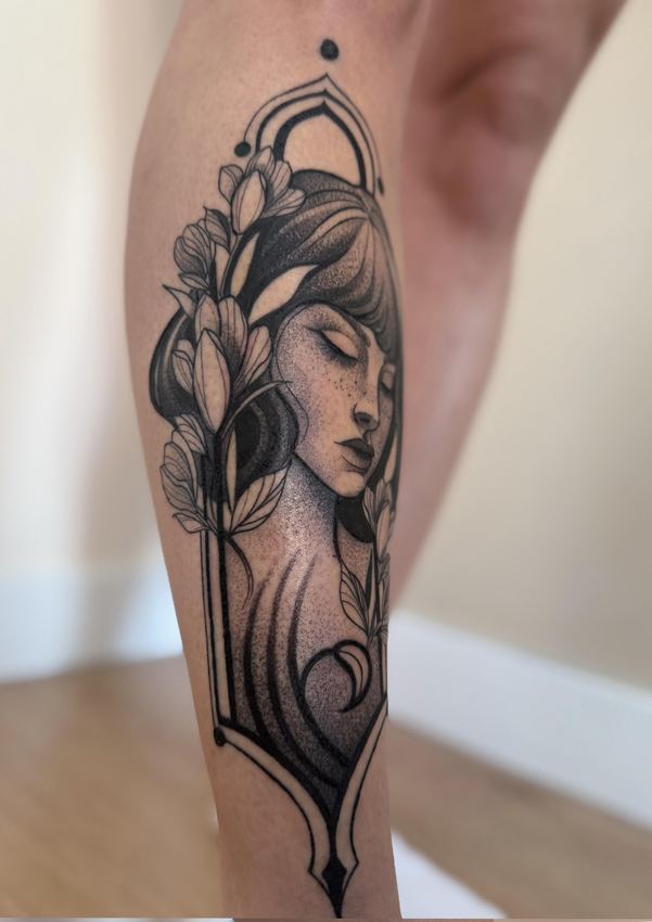 Tatuaje blackwork estilo art nouveau con el rostro de una mujer entre magnolias, en el gemelo