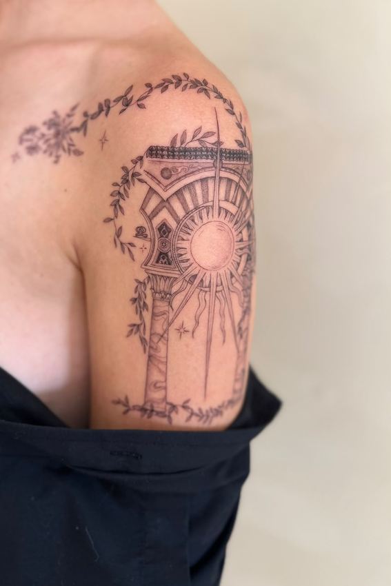 Tatuaje fine line de una torre con un sol radiante rodeada de enredadera floral, en el hombro