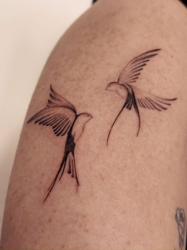 Tatuaje fine line de dos golondrinas en vuelo, en el muslo