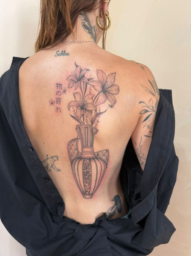 Tatuaje fine line de un jarrón ornamental con lirios en el centro de la espalda