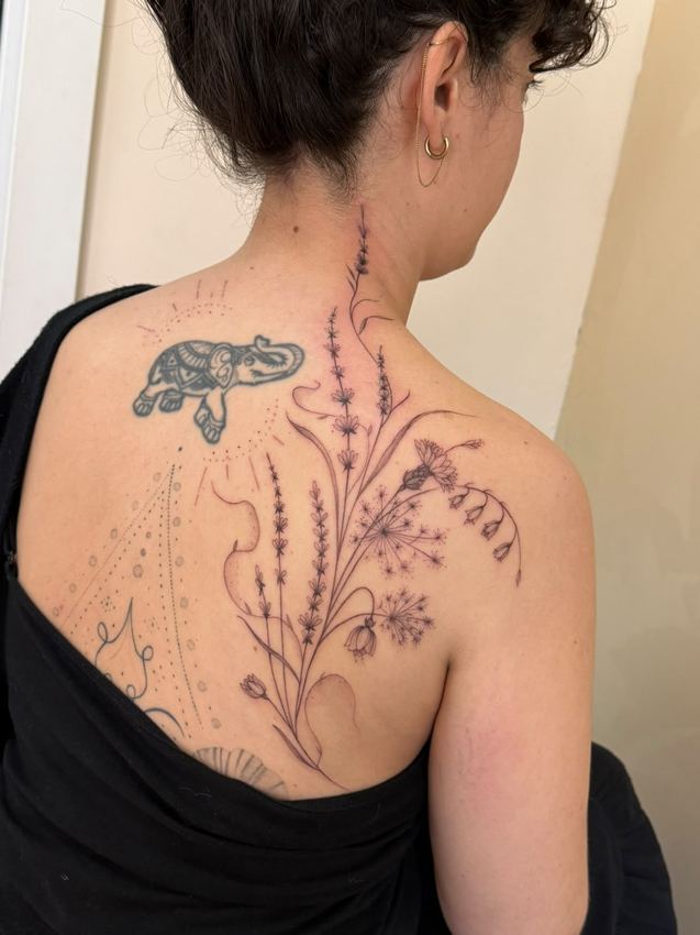 Tatuaje fine line de ramas de lavanda sobre el omóplato y la columna