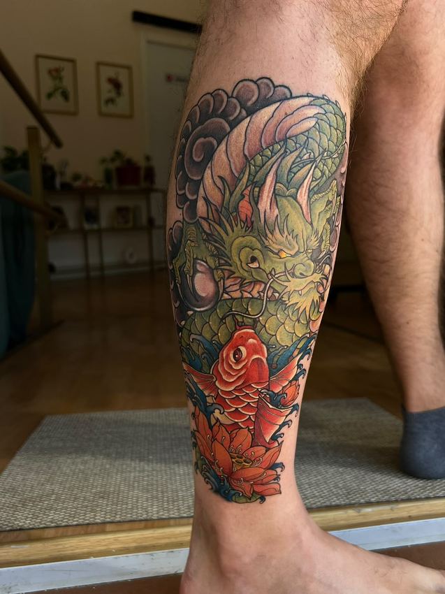 Tatuaje japonés a color con un dragón verde y una carpa koi roja entre olas, en la pierna