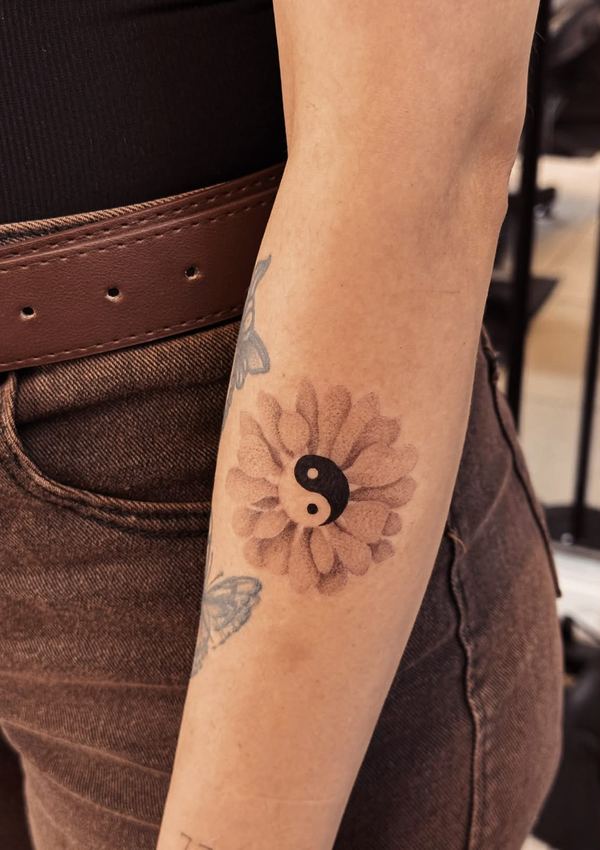 Tatuaje de una margarita con un símbolo yin-yang en el centro, en el brazo