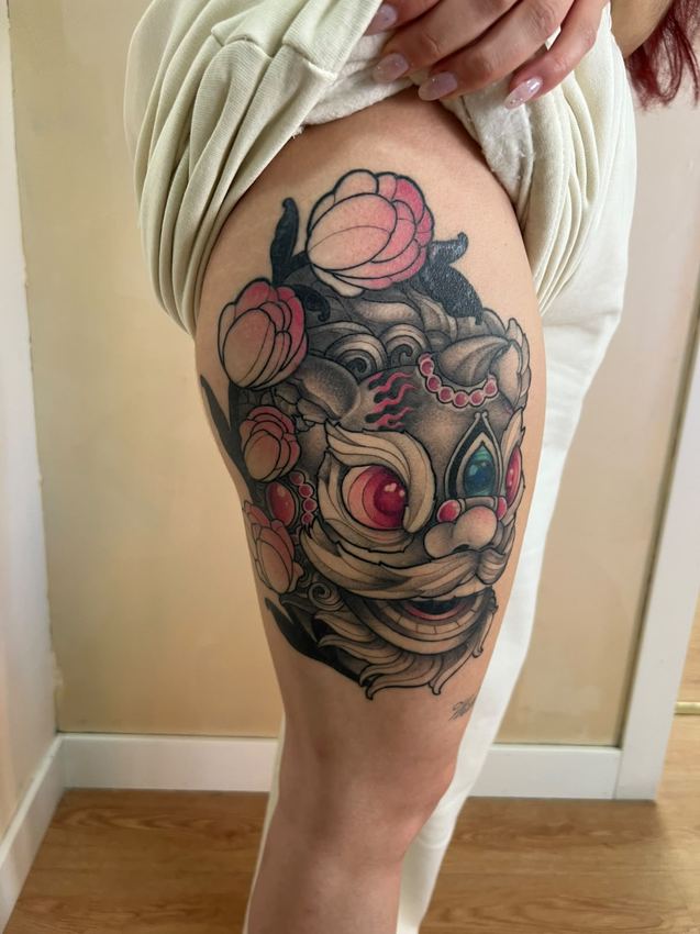 Tatuaje neotradicional de una máscara hannya rodeada de peonías, en el muslo