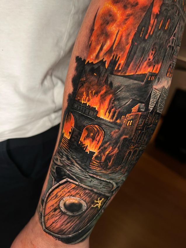 Tatuaje realista a color de una ciudad en llamas sobre el agua, en el antebrazo
