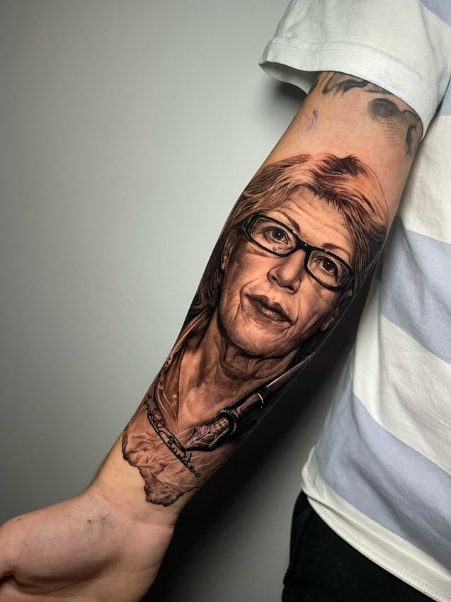 Tatuaje de realismo en blanco y negro con el retrato de una mujer con gafas, en el antebrazo